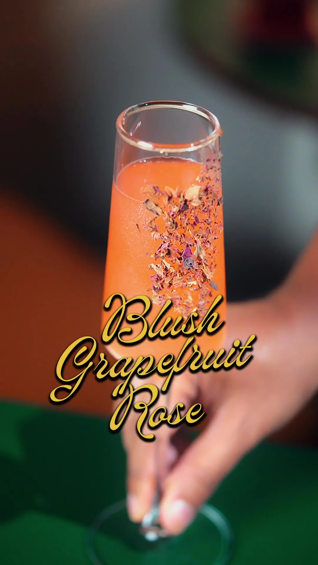 A tall glass of grapefruit-pink cocktail garnished with dried flowers, captioned "Blush Grapefruit Rose."