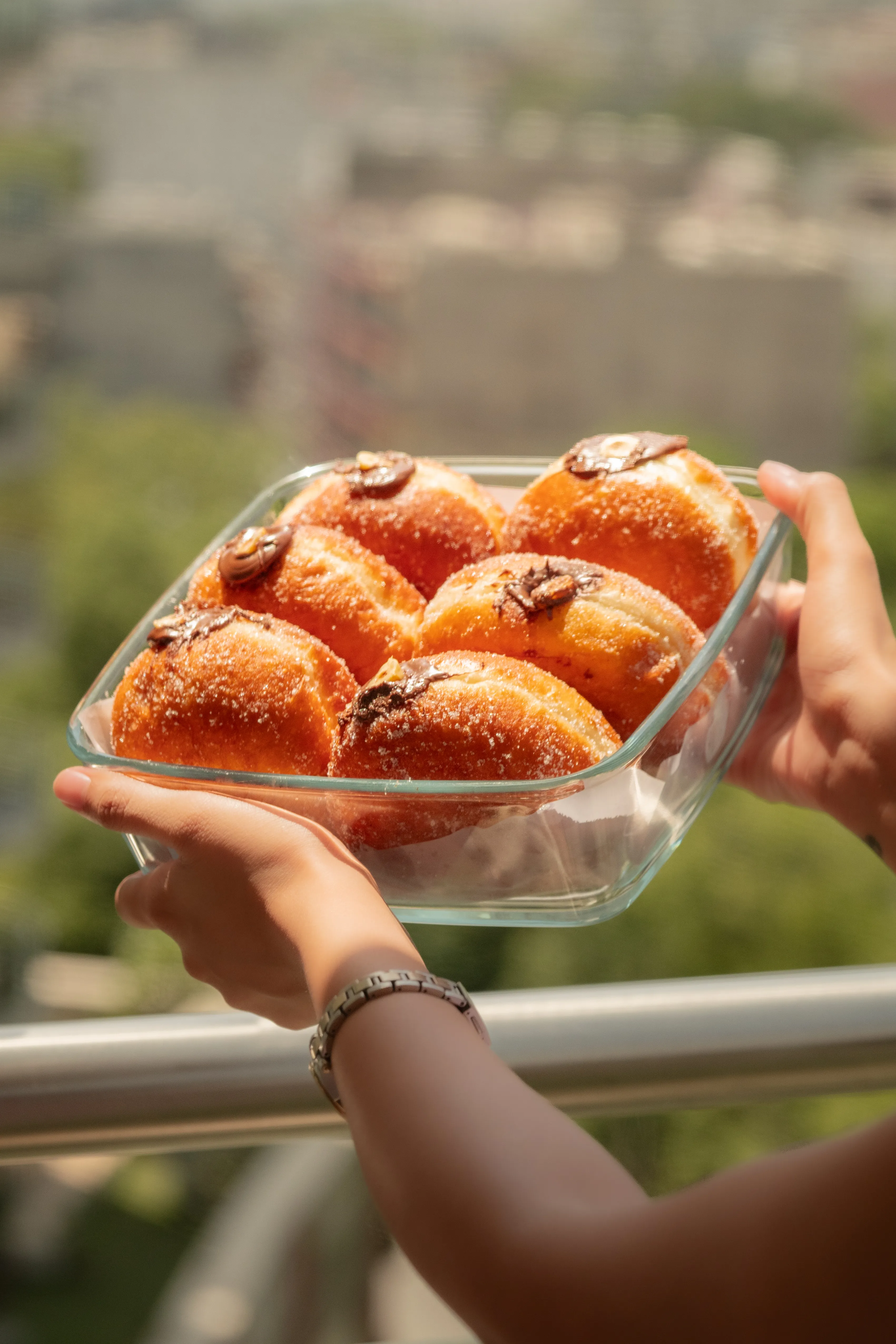 The same tray of sugared, Nutella-filled bomboloni, held up against a blurred cityscape.