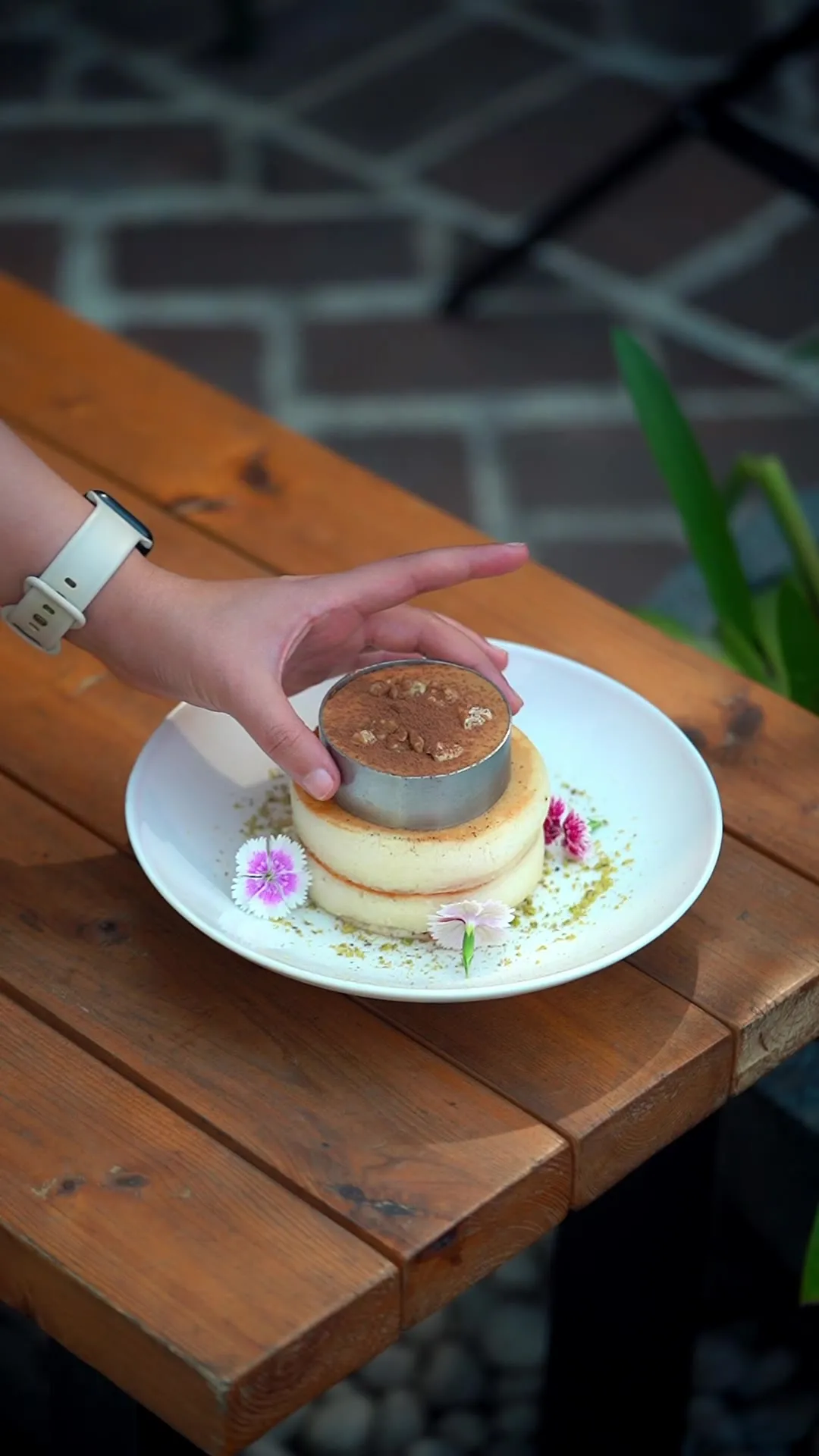 A hand pressing into a stacked pudding-and-pancake dessert garnished with edible flowers.