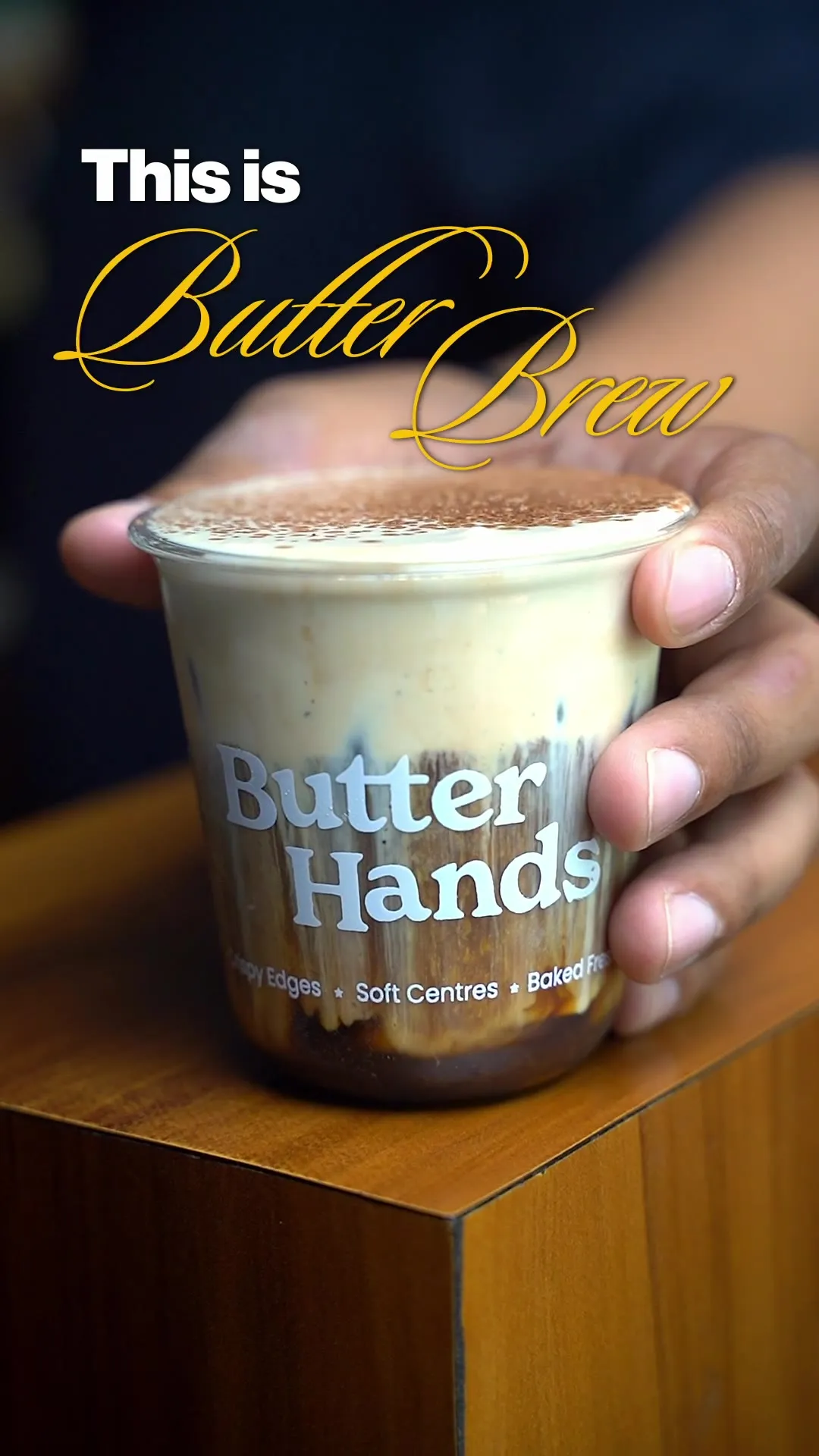 A hand holding a "Butter Brew" branded takeaway cup of frothy coffee.