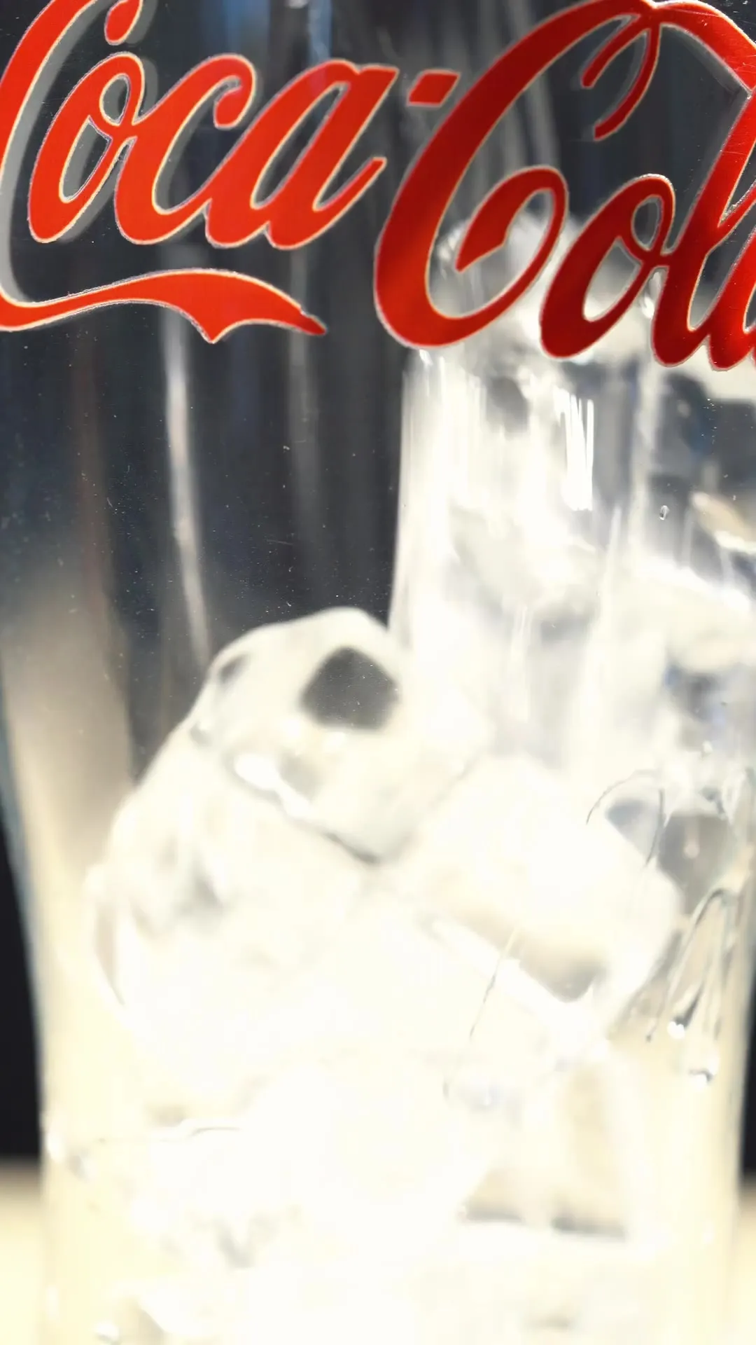 A close-up of ice and fizzy dark soda in a glass.