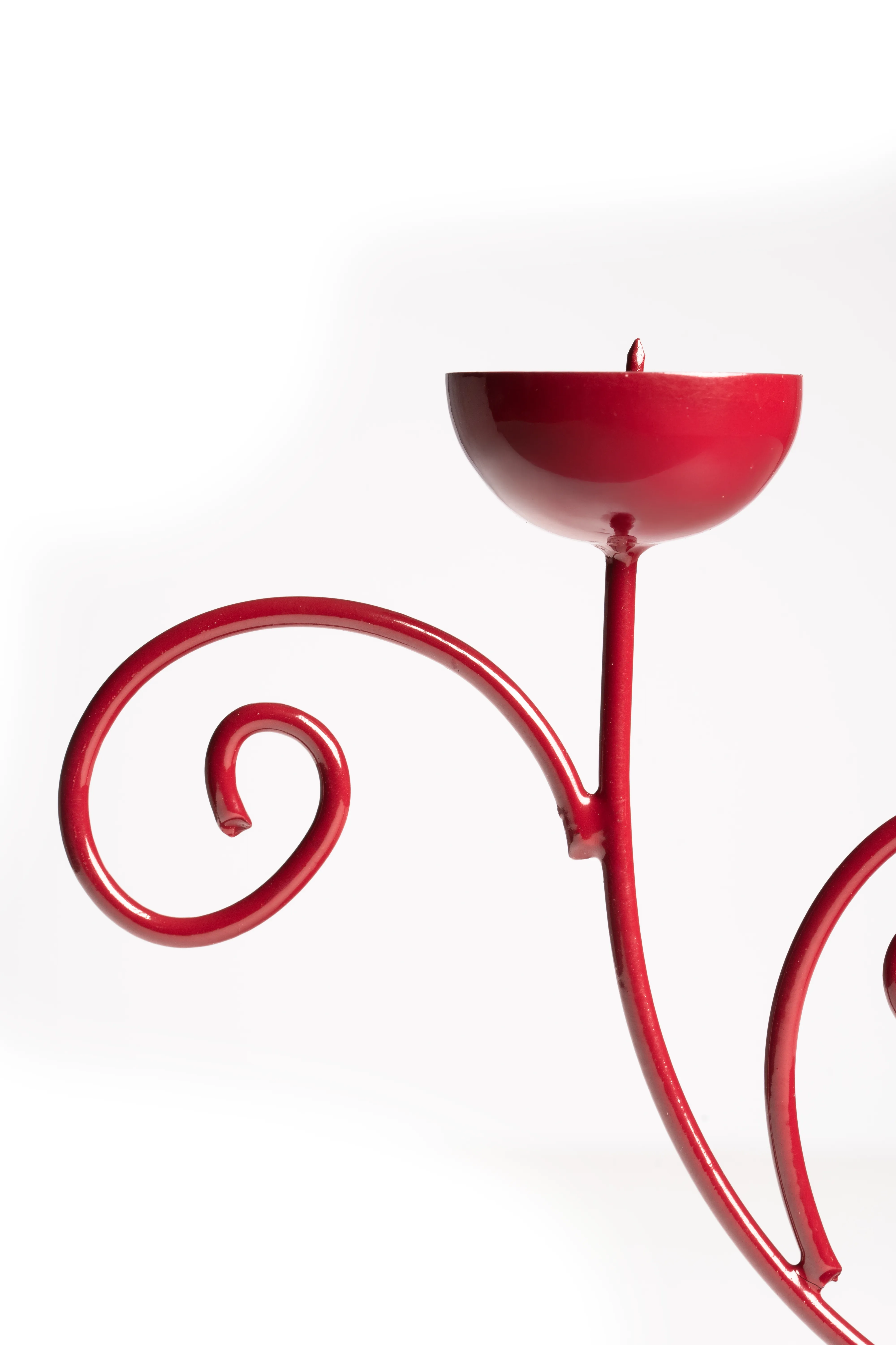 A close-up of the red scrollwork double candle holder's cup and curled arm against a white background.