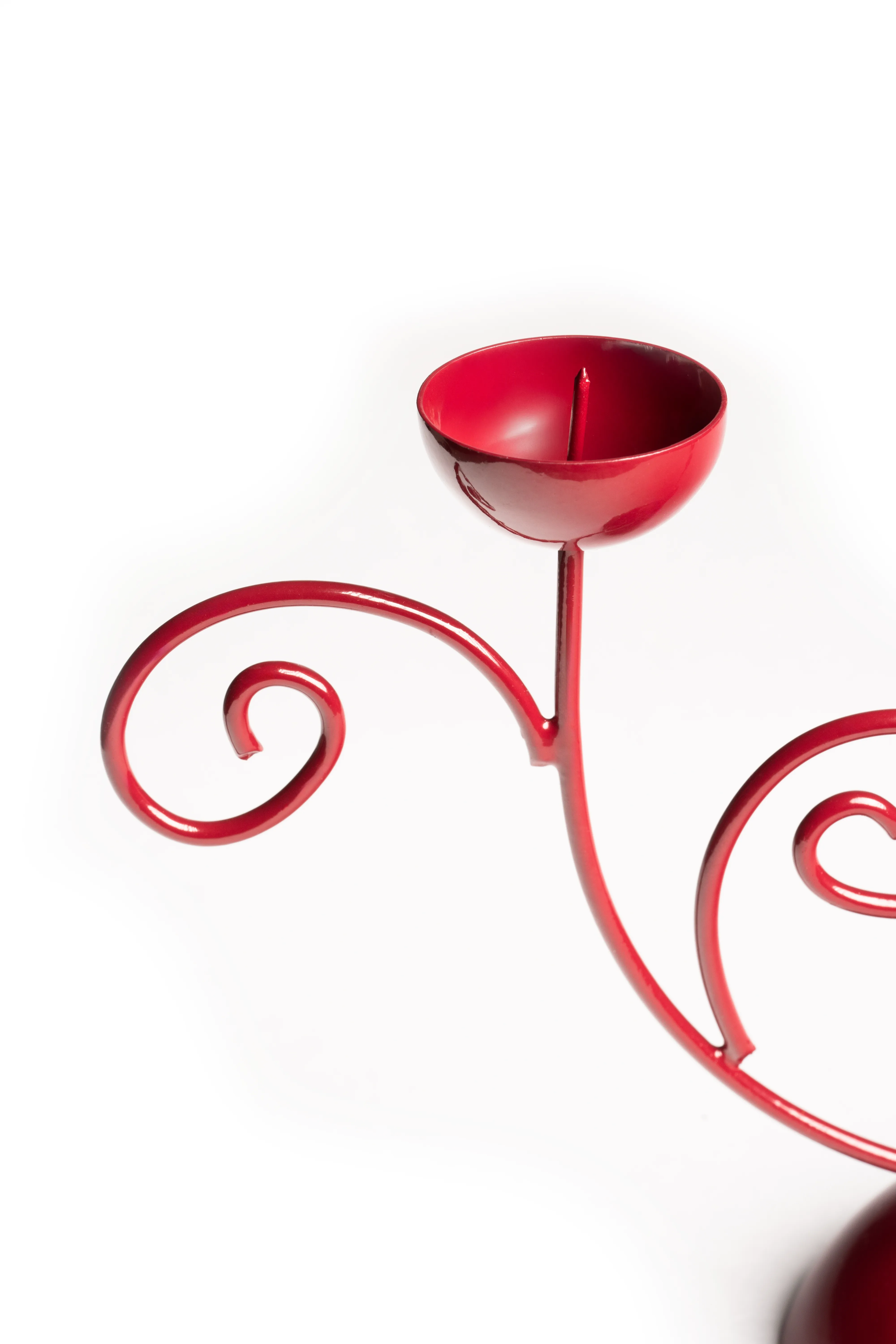 A close-up of the red scrollwork double candle holder's empty candle cup and curled metal arms against a white background.