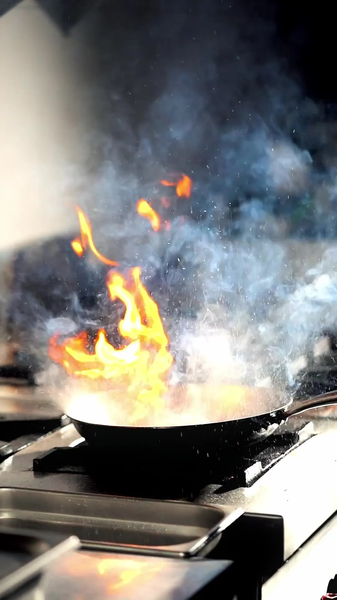 A pan of food catching flame over high heat in the kitchen.