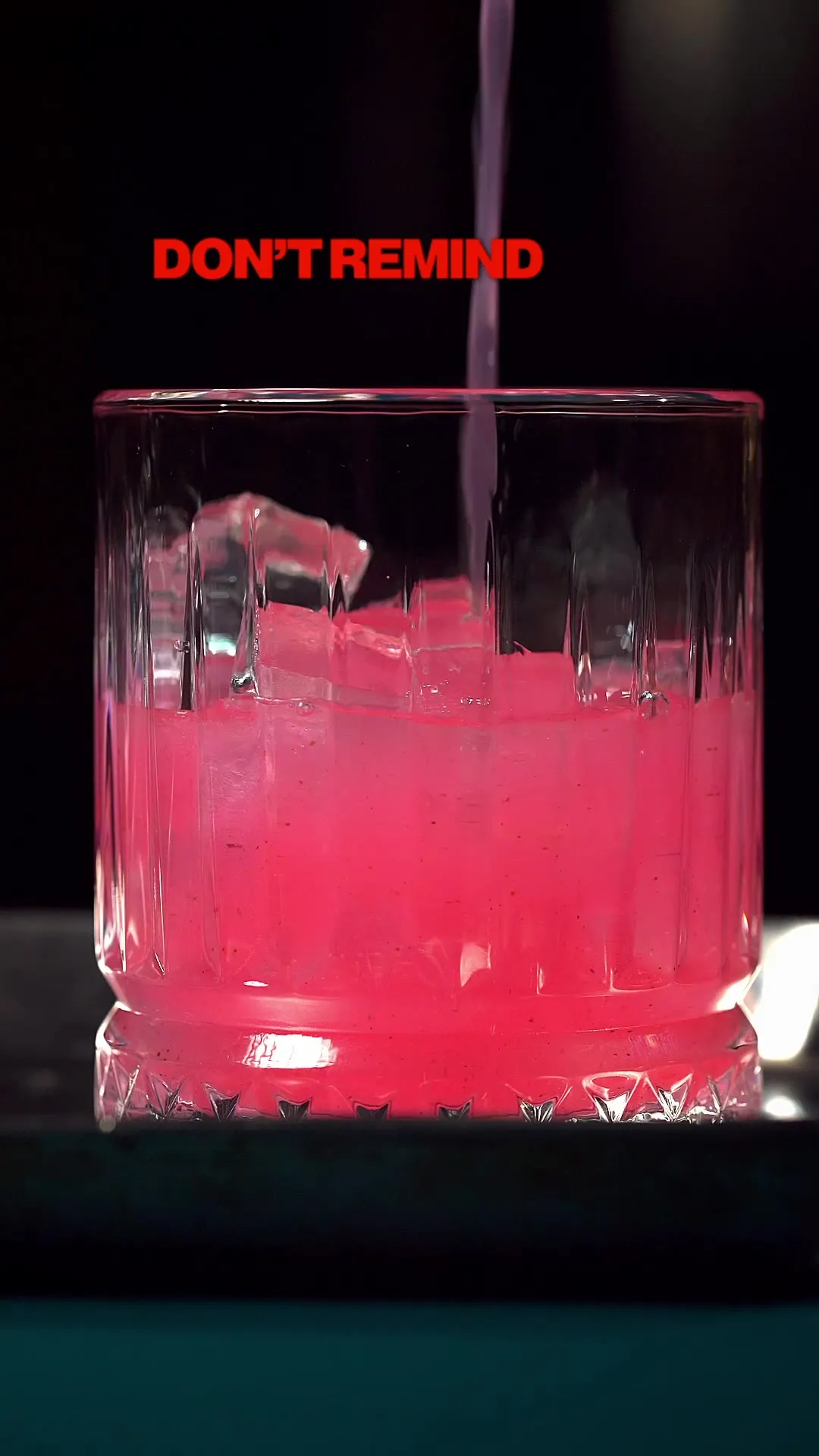 A pink cocktail being poured over ice in a glass.