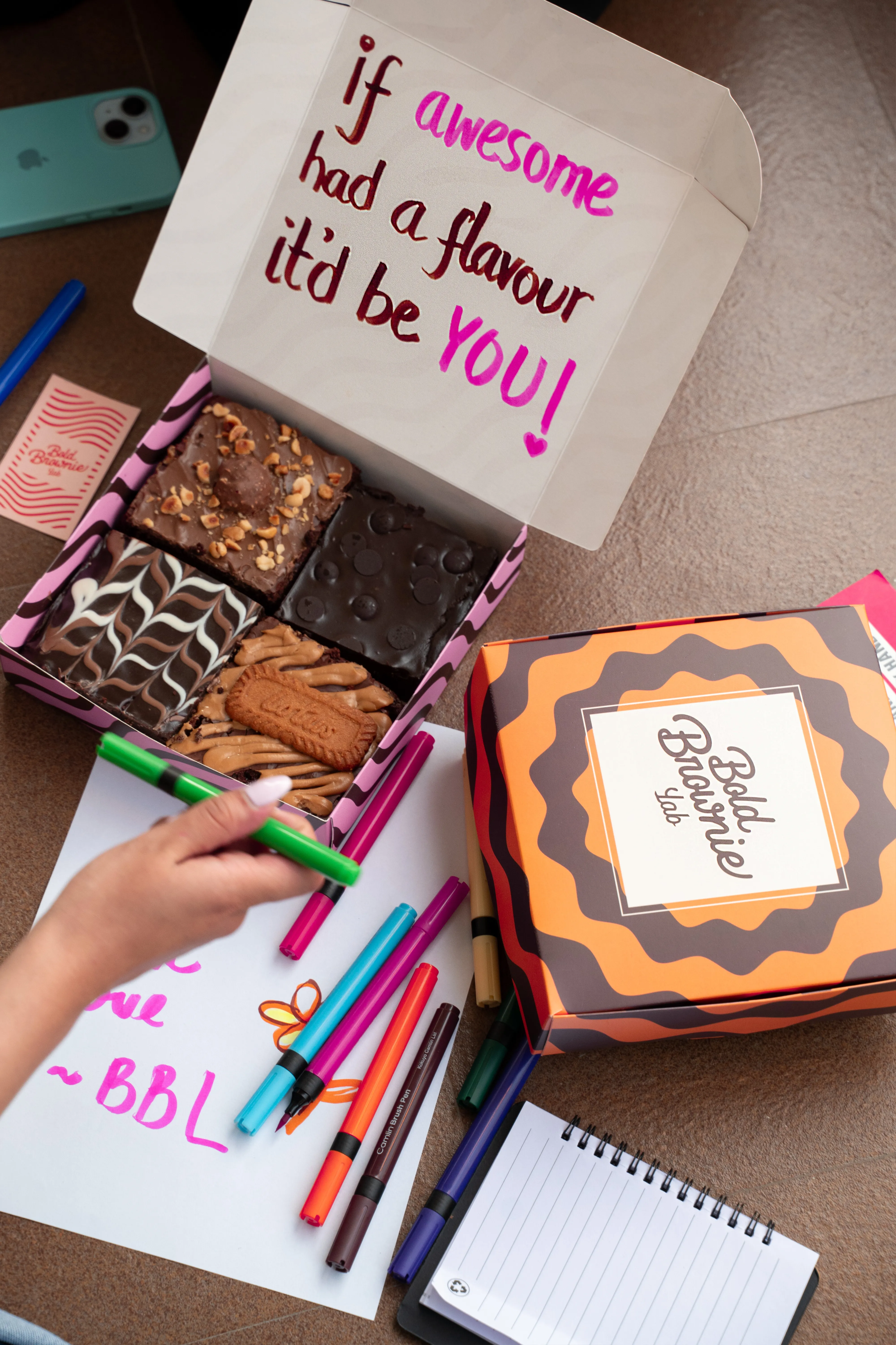 An open Bold Brownie Lab box beside a handwritten note reading "if awesome had a flavour it'd be YOU! ~ BBL," with a second box and colored brush pens scattered around.