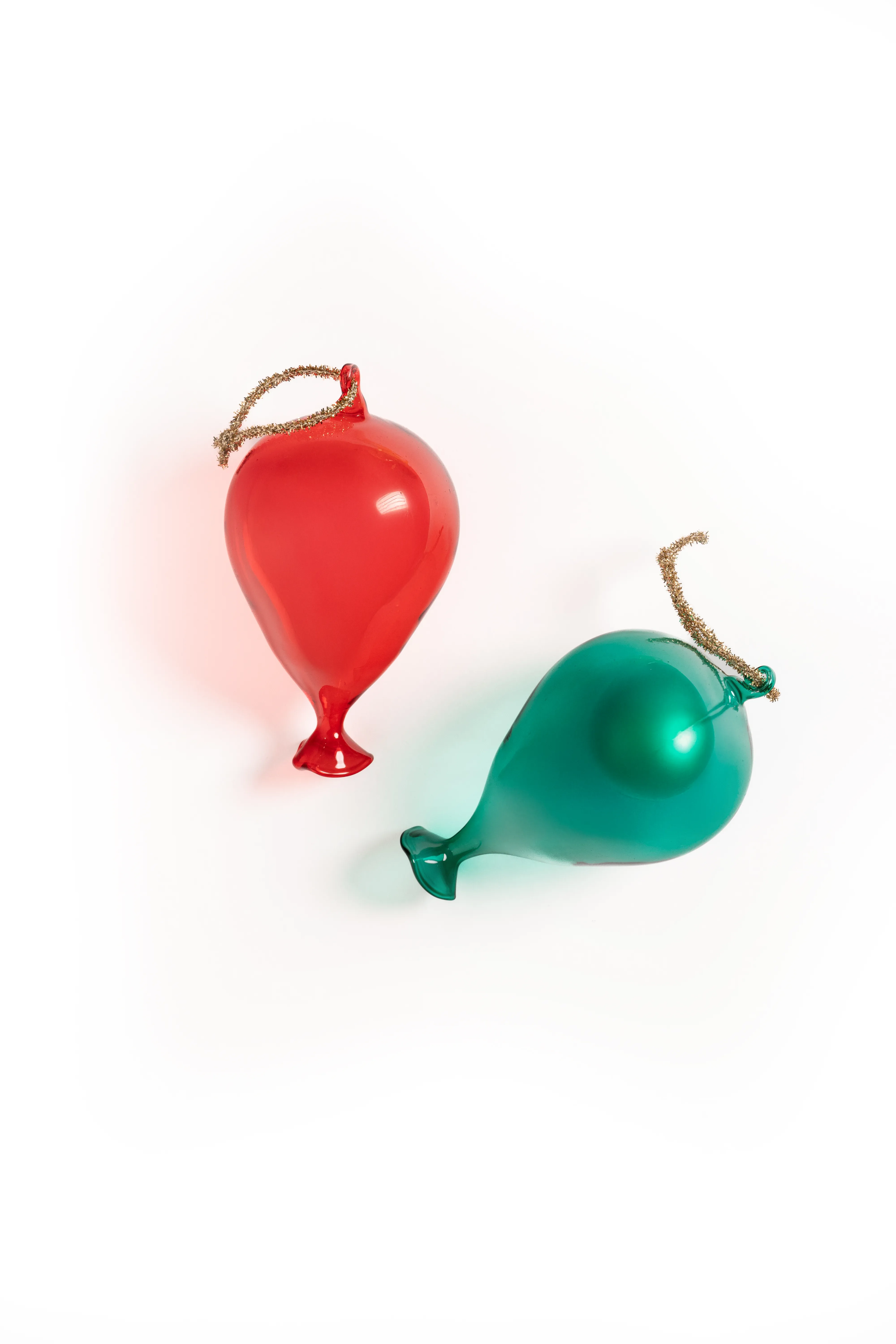 A red and a green glass balloon-shaped ornament on gold cords, lying against a white background.