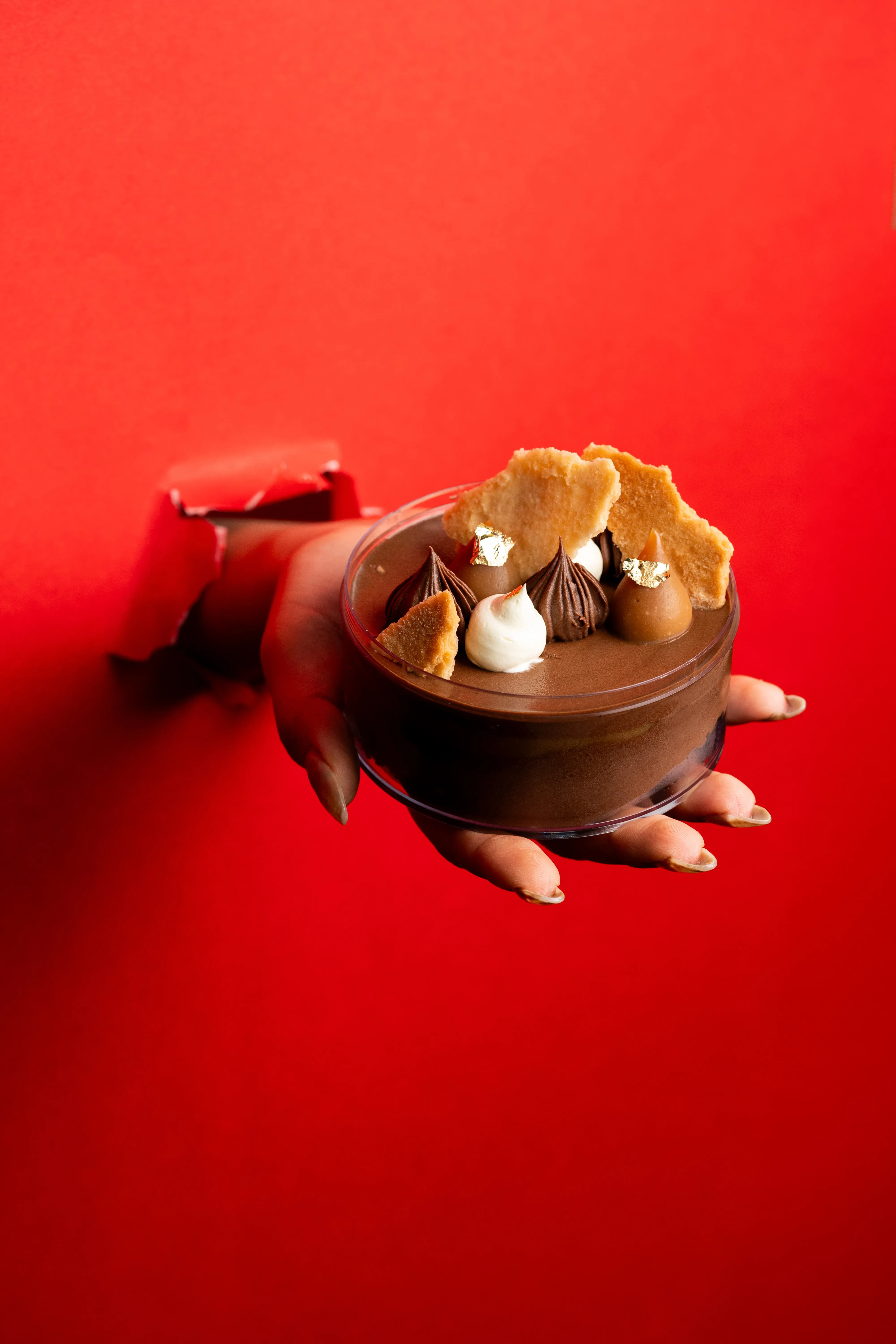 A closer view of the chocolate mousse dessert held through the torn red paper.
