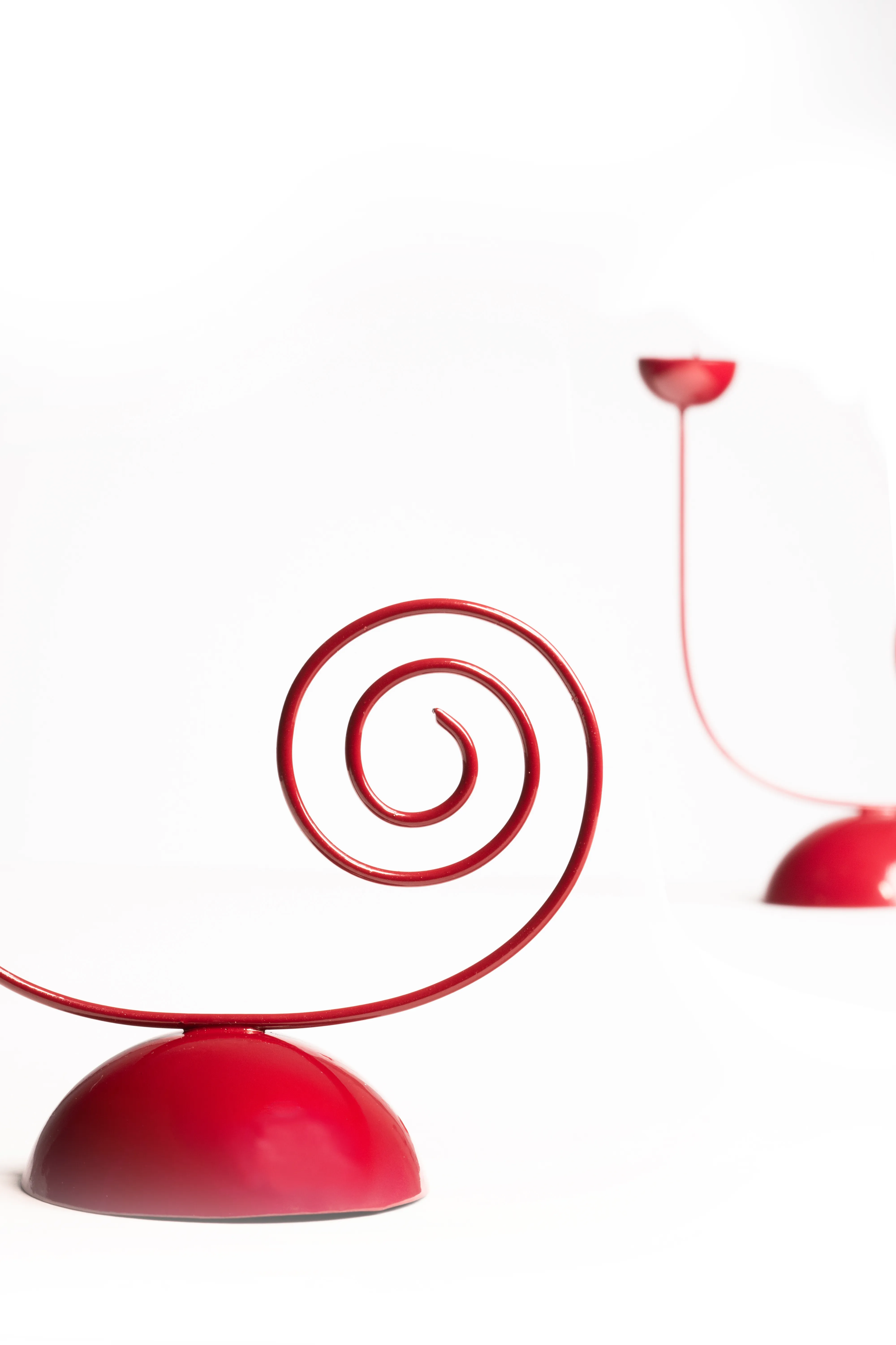 Two red spiral-base single candle holders, one in focus in the foreground, against a white background.