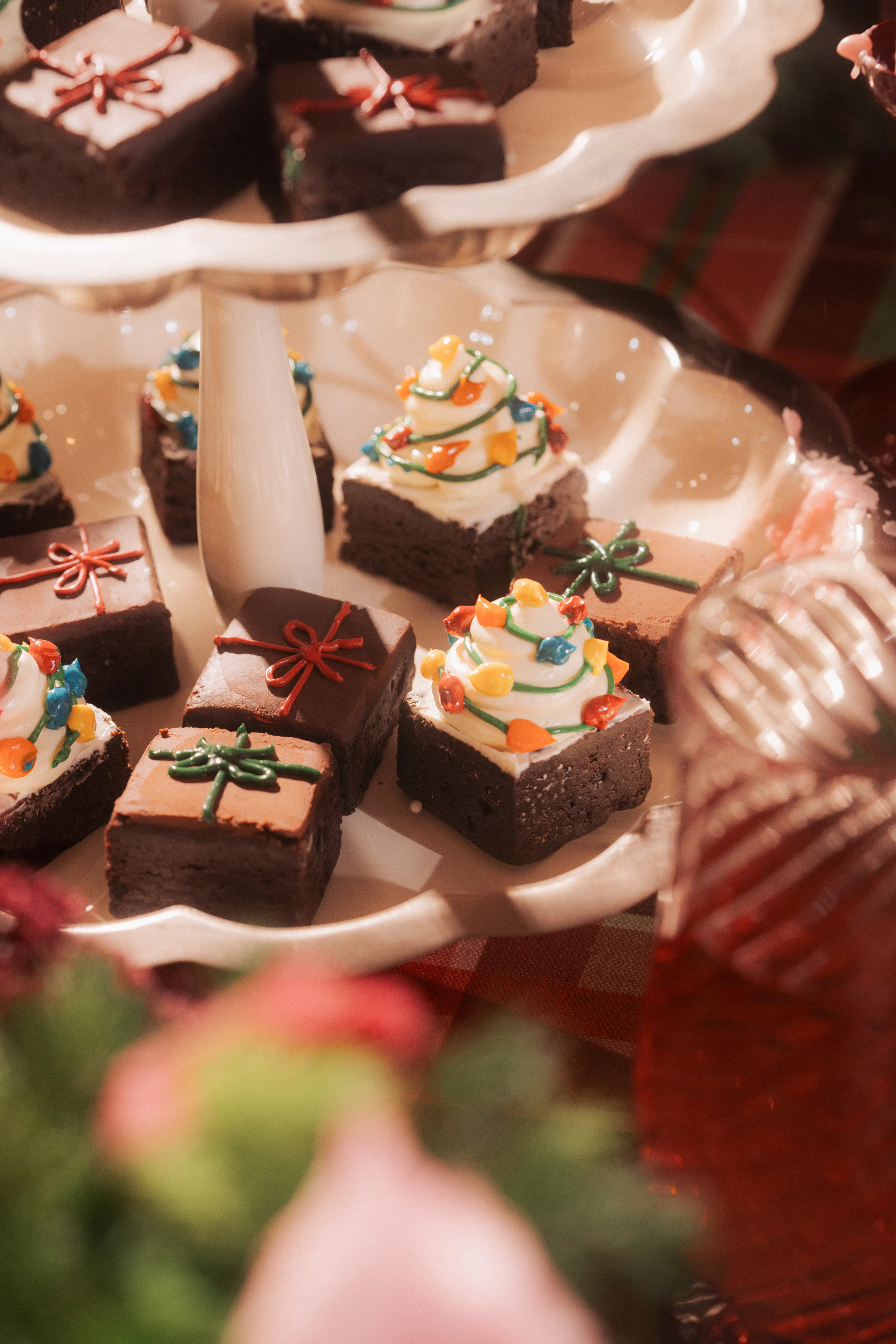 A tiered stand of gift- and tree-decorated brownie bites beside a glass and pink roses.