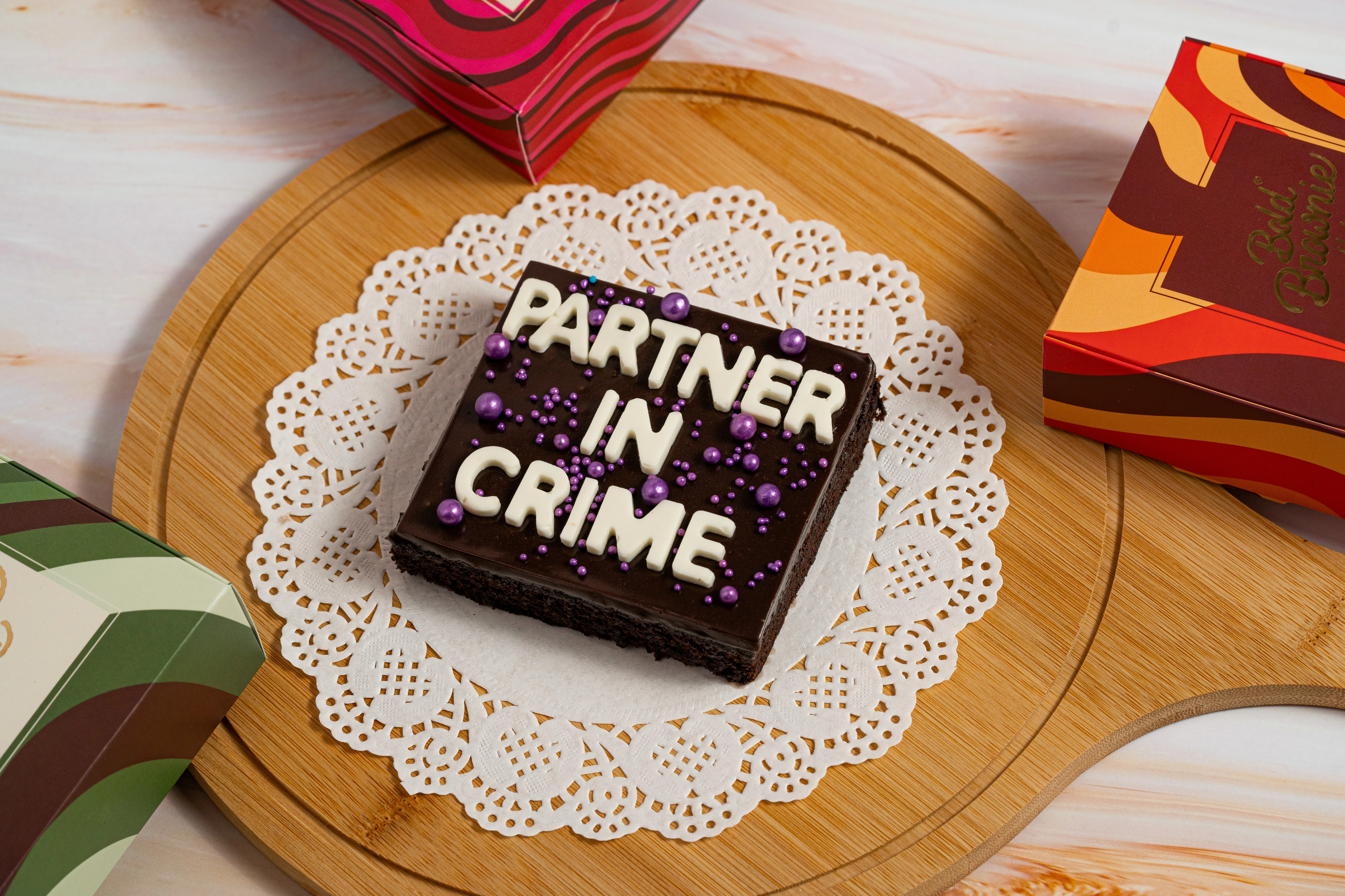 A hand holding a stack of four colorful Bold Brownie Lab boxes topped with a walnut brownie, against a white background.