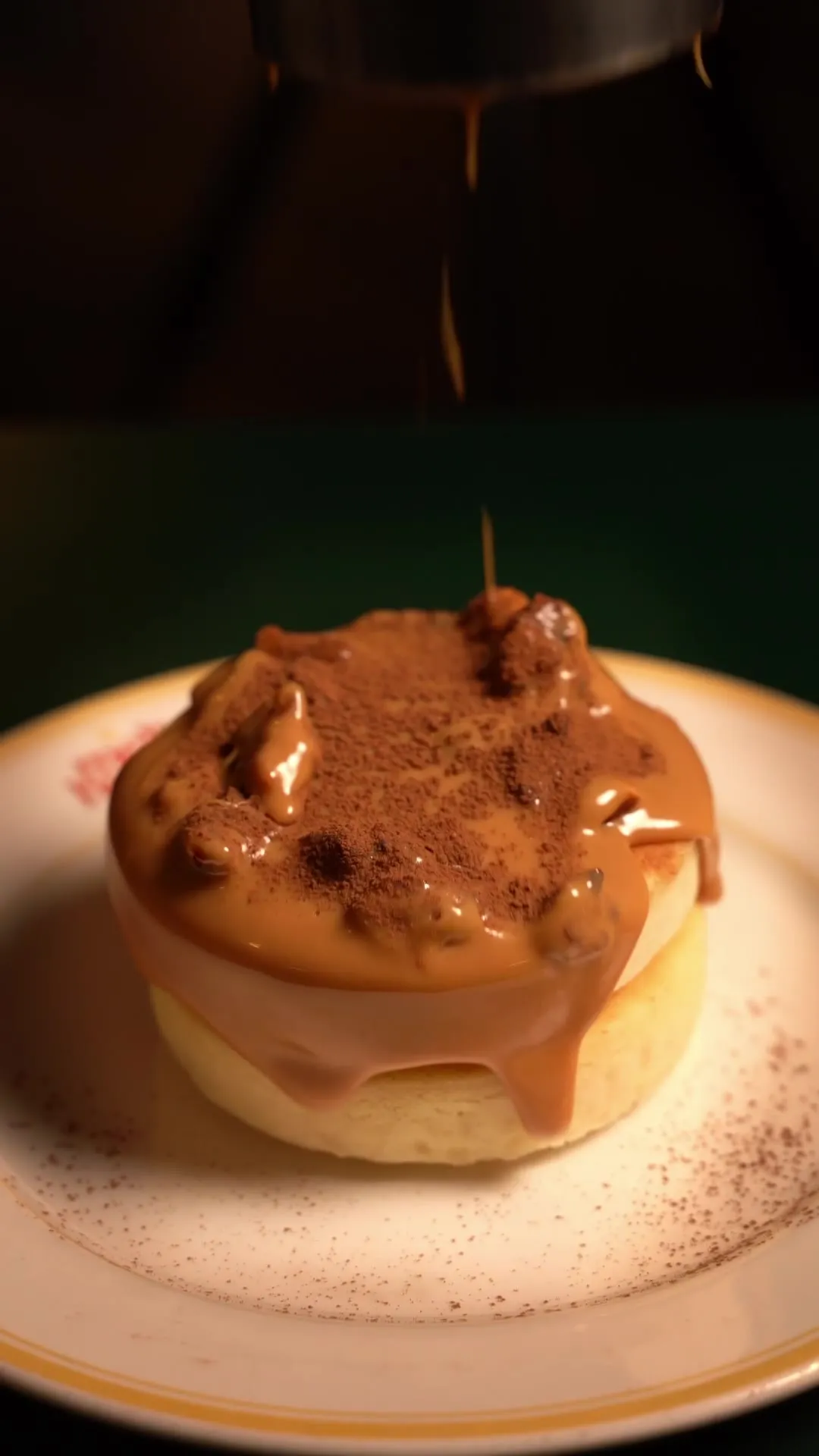 Toffee sauce drizzling over a stacked pancake dessert dusted with cocoa and walnuts.