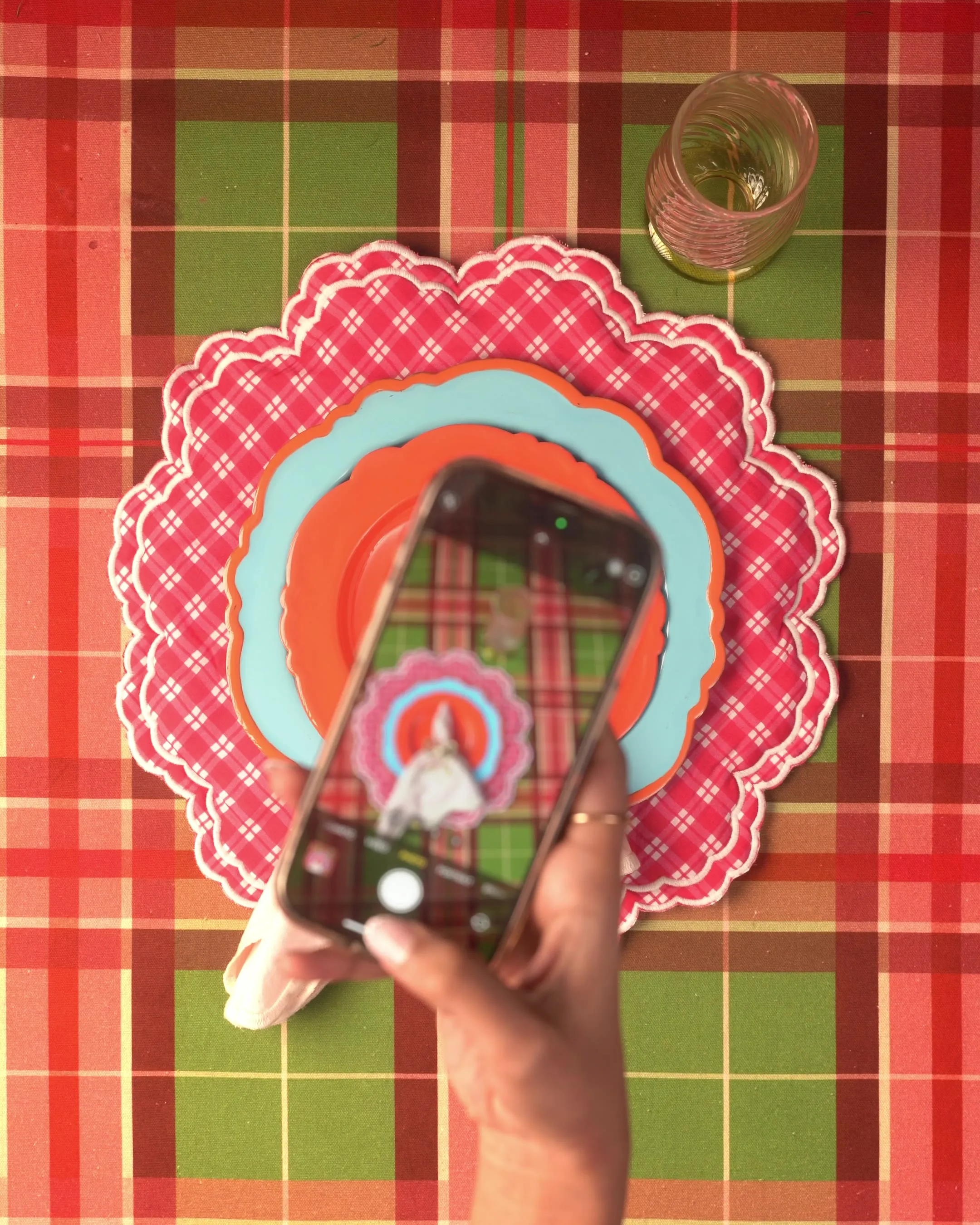 An overhead view of a hand photographing a plated dessert on a scalloped placemat with a phone.