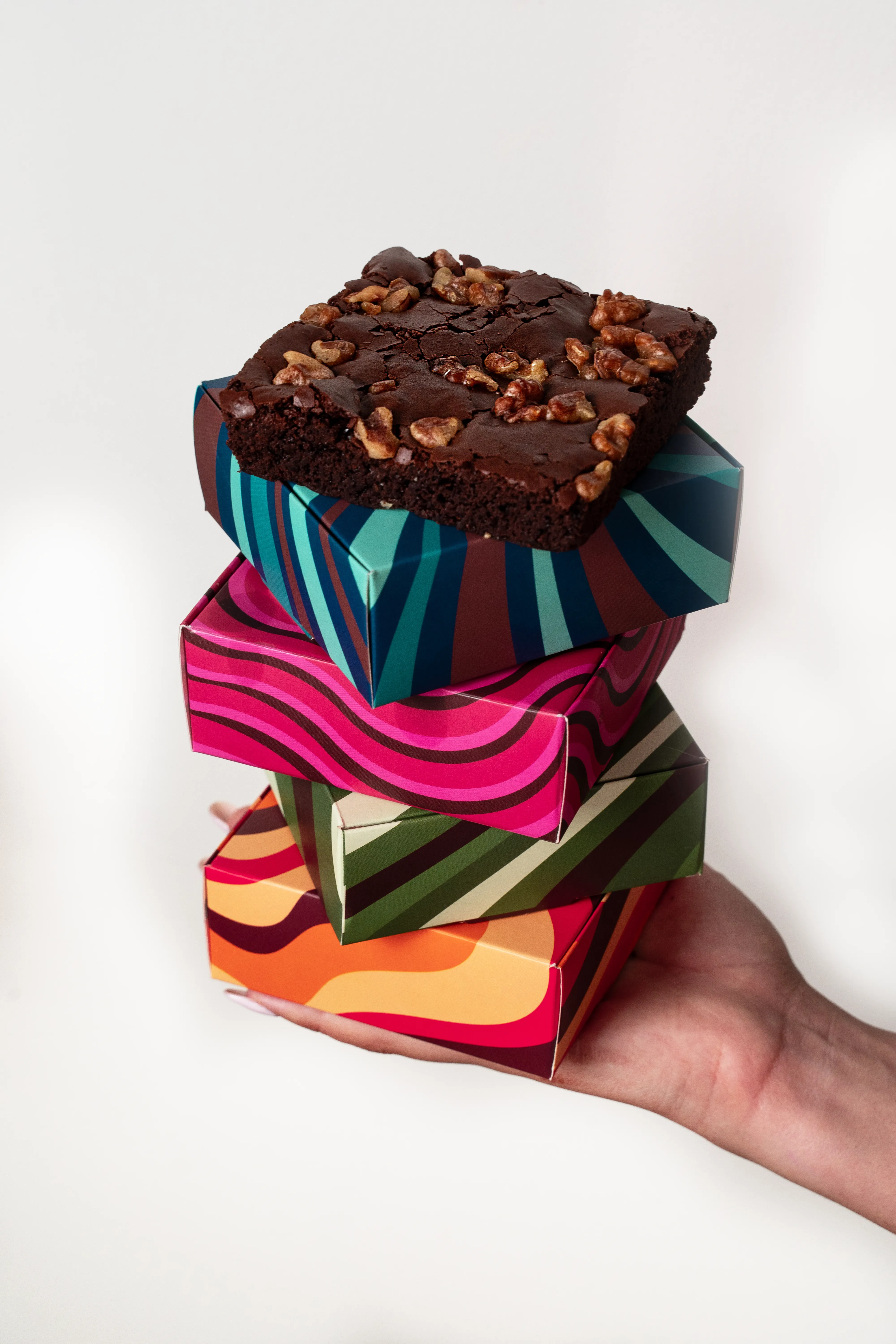 A brownie drizzled with a wavy line of melted chocolate and scattered hazelnuts, plated on a marble surface.