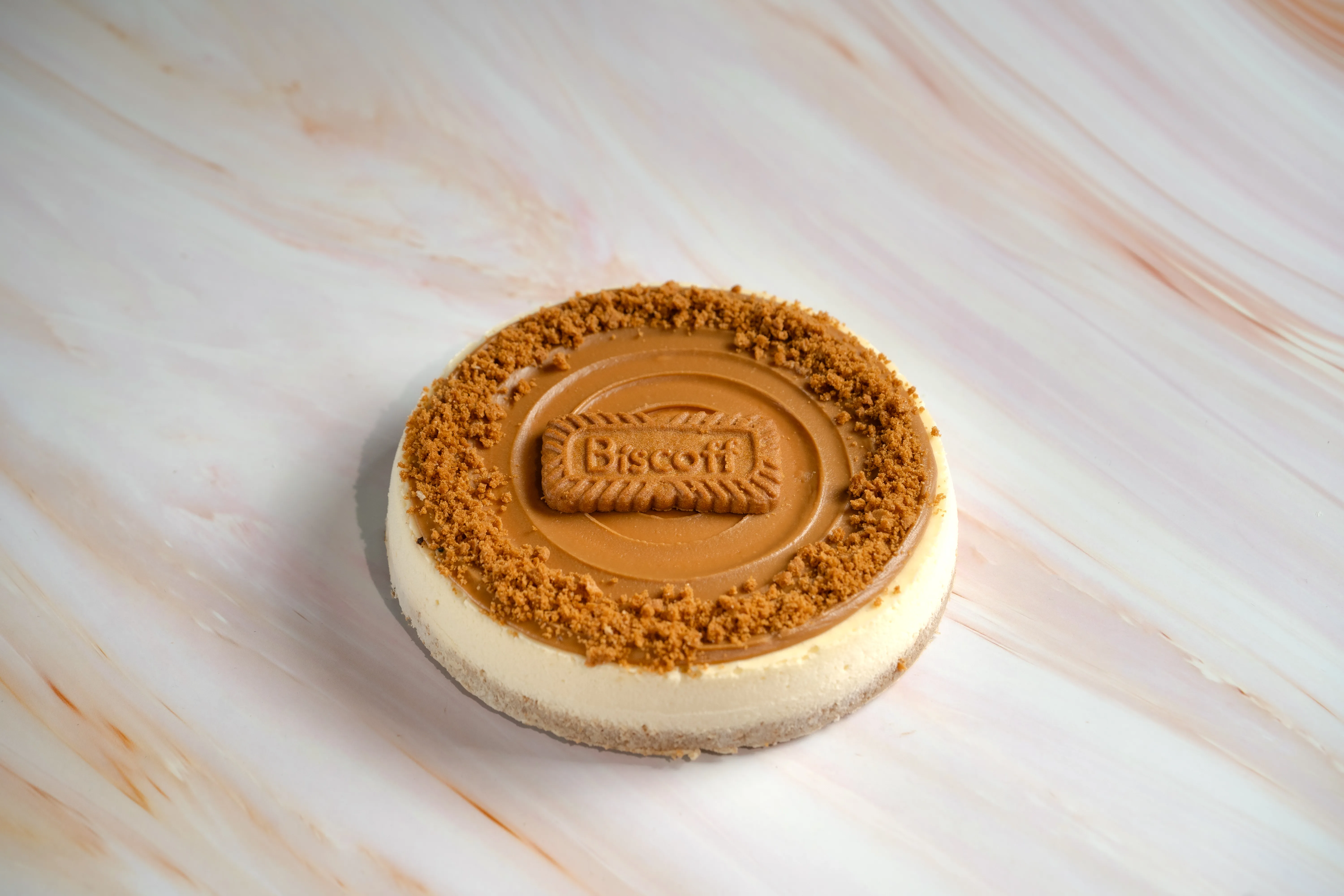 A round Biscoff cheesecake topped with caramel, a Biscoff cookie, and cookie crumbs.