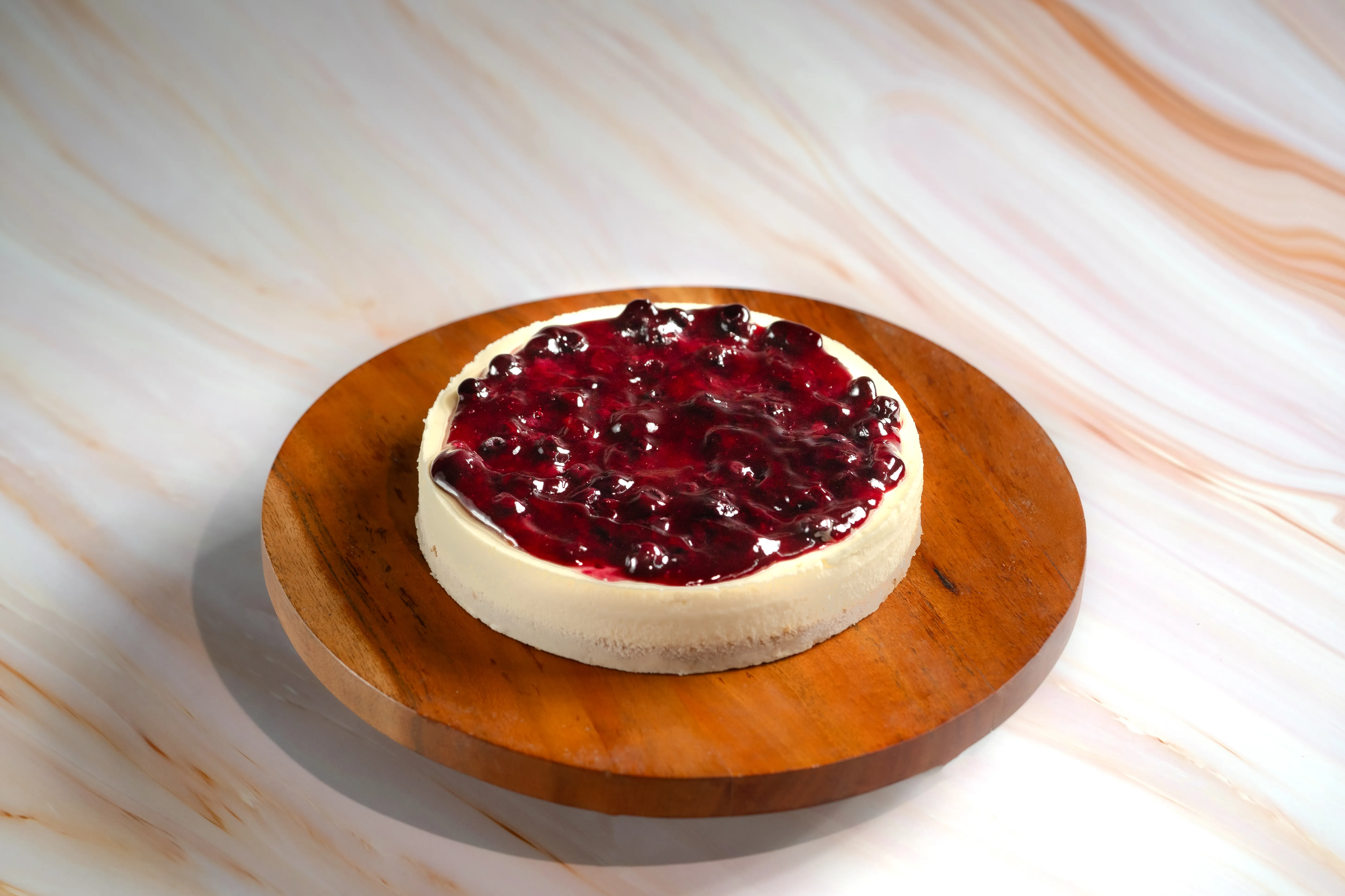 A round cheesecake topped with a glossy mixed-berry compote, on a wooden board.